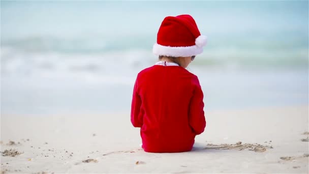 Back view of adorable girl in Christmas hat on white beach during Xmas vacation — Stock Video