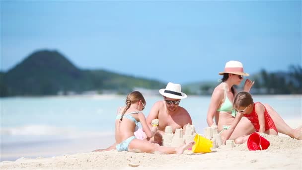 Familia de cuatro haciendo castillo de arena en la playa tropical blanca — Vídeos de Stock