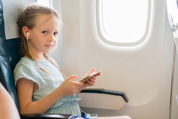 Adorable niñita viajando en un avión. Lindo niño con portátil cerca de la ventana en avión — Foto de Stock