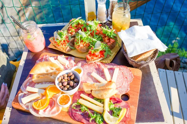 Tasty italian snack. Fresh bruschettes, cheeses and meat on the board in outdoor cafe with amazing view in Manarola, Italy — Stock Photo, Image