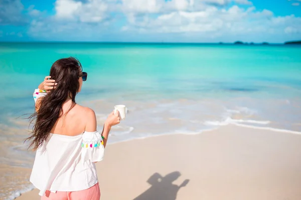ビーチで若い女性。海岸に一杯のコーヒーと少女の背面図 — ストック写真