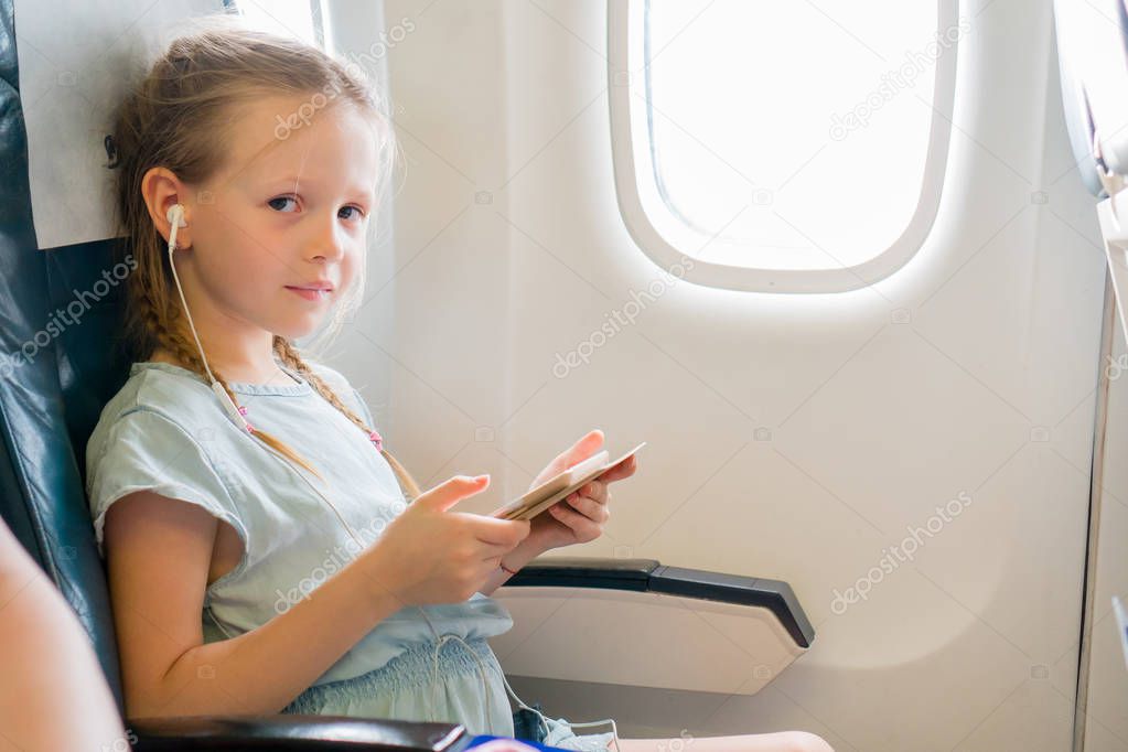 Adorable little girl traveling by an airplane. Cute kid with laptop near window in aircraft