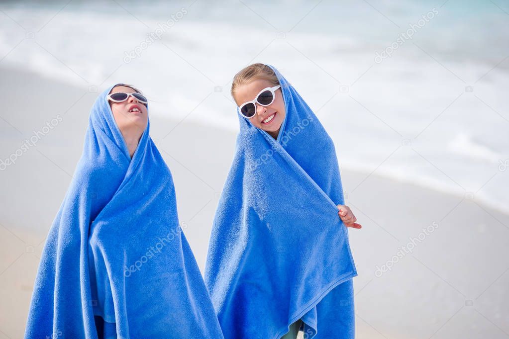 Adorable little girls wrapped in towel at tropical beach after swimming in the sea. Two sisters playing on the beach, beach towels