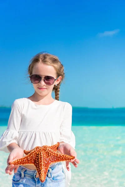 Adorável menina com estrela do mar na praia branca vazia — Fotografia de Stock