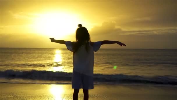 Adorable niña feliz en la playa blanca al atardecer. Silueta de niña en la costa en una hermosa puesta de sol — Vídeo de stock