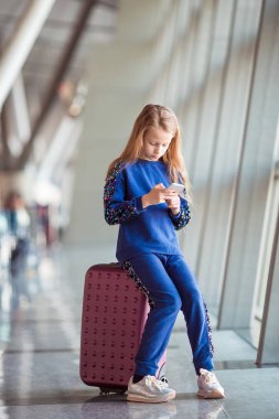 Havaalanındaki küçük sevimli kız büyük pencerenin yanında telefonuyla oynuyor.
