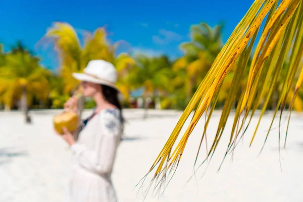 Mujer joven bebiendo leche de coco en un día caluroso en la playa. Hojas de palmera de primer plano — Foto de Stock