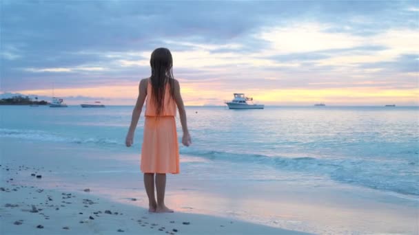 Gün batımında beyaz sahilde sevimli, mutlu küçük bir kız.. — Stok video