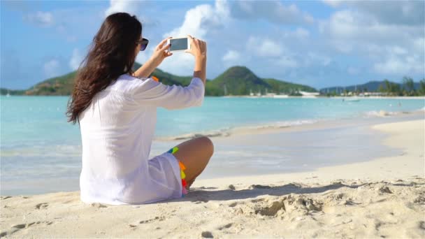 Genç bir kadın beyaz kumda uzanıyor ve telefonuyla konuşuyor. — Stok video