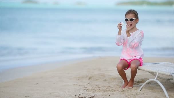 Счастливая маленькая девочка с игрушечным самолетом в руках на белом песчаном пляже. Детские игры с игрушками на пляже — стоковое видео