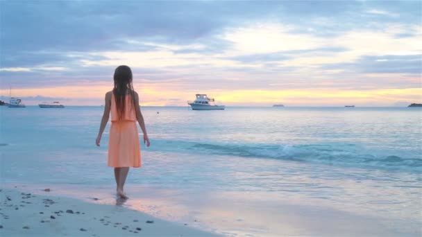 Entzückend glückliches kleines Mädchen am weißen Strand bei Sonnenuntergang. — Stockvideo