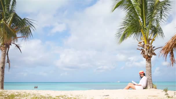 Genç bir kadın, tropikal beyaz kumsalda kitap okuyor. — Stok video