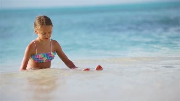 Liebenswertes kleines Mädchen am Strand, das viel Spaß im seichten Wasser hat — Stockvideo