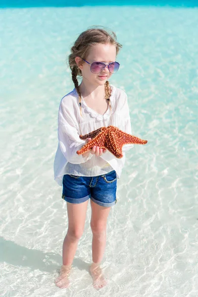 Entzückendes kleines Mädchen mit Seesternen am Strand — Stockfoto
