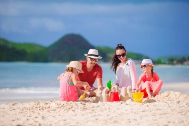 Tropik beyaz sahilde kumdan kale yapan dört kişilik bir aile.