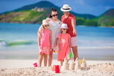 Tropik beyaz sahilde kumdan kale yapan dört kişilik bir aile.