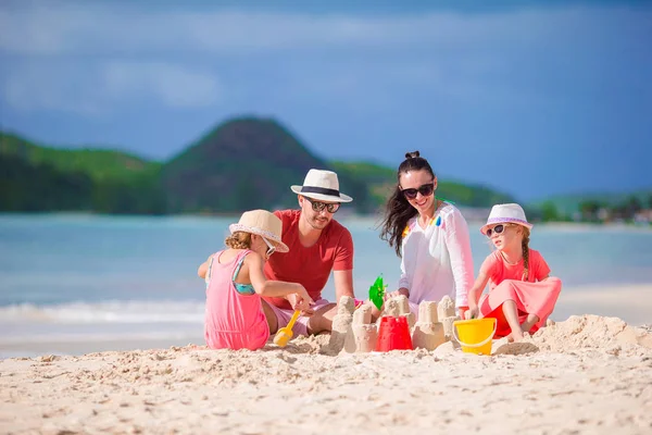 Tropik beyaz sahilde kumdan kale yapan dört kişilik bir aile.