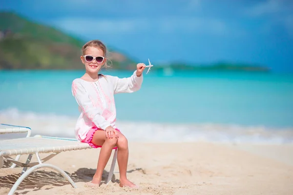 Glückliches kleines Mädchen mit Spielzeugflugzeug in der Hand am weißen Sandstrand. — Stockfoto