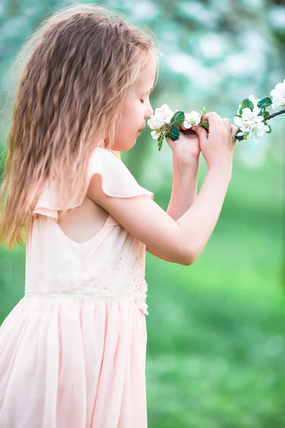 Pieni kaunis tyttö nauttii tuoksu kukkiva kevät puutarha — kuvapankkivalokuva