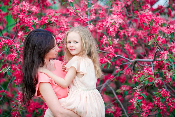 Entzückendes kleines Mädchen mit junger Mutter im blühenden Kirschgarten am Frühlingstag — Stockfoto