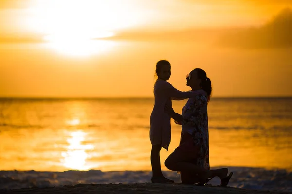 Маленька дівчинка і щаслива мати силует на заході сонця на пляжі — стокове фото