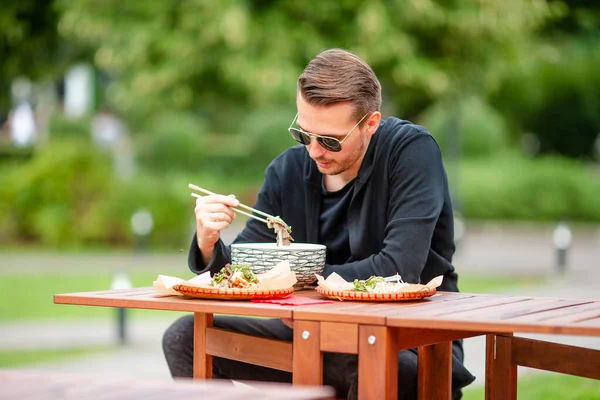 Young man eating take away noodles on the street — Stock Photo, Image