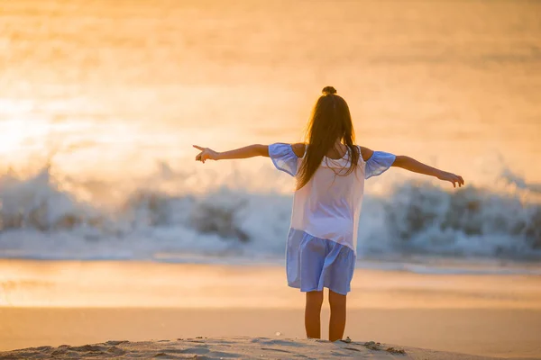 Очаровательная счастливая маленькая девочка, гуляющая по белому пляжу на закате . — стоковое фото