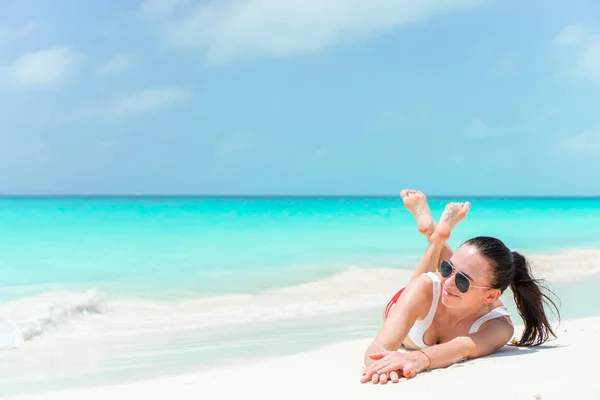 Gelukkig jongedame in zwembroek op witte strand. Mooi model in bikini zitten. — Stockfoto
