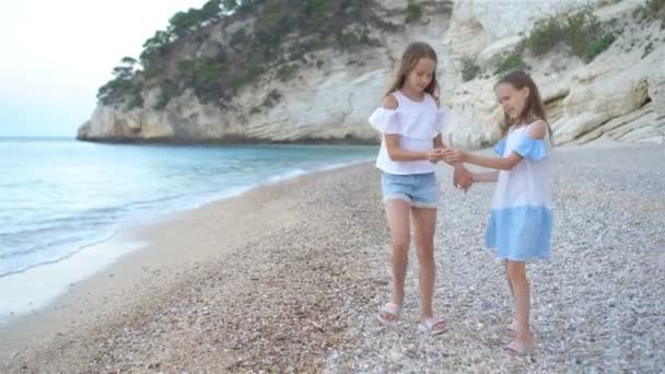 Piccole ragazze divertenti felici si divertono molto alla spiaggia tropicale a giocare insieme. Giorno soleggiato con pioggia nel mare — Video Stock