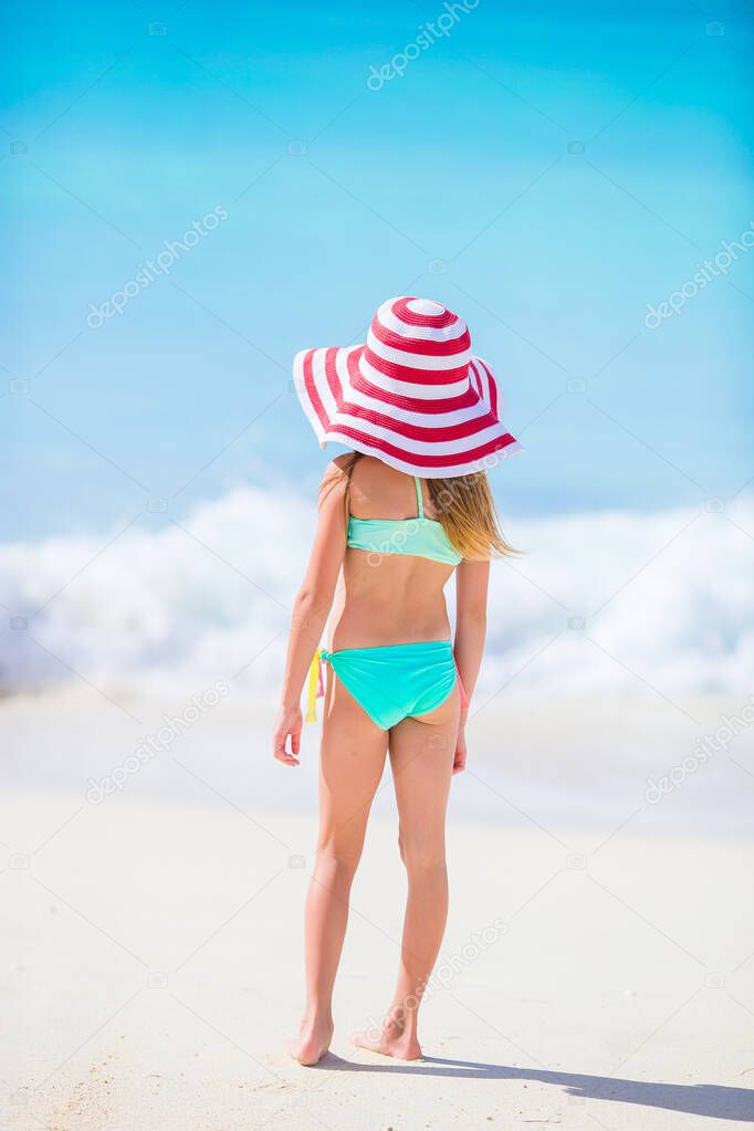 Adorable little girl in big red hat walking along white sand Caribbean beach
