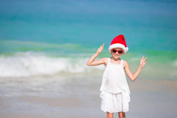 Entzückendes kleines Mädchen mit Weihnachtsmütze am tropischen Strand — Stockfoto