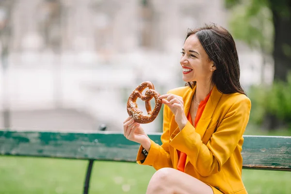 Schöne junge Frau hält Brezel in der Hand und entspannt sich im Park — Stockfoto