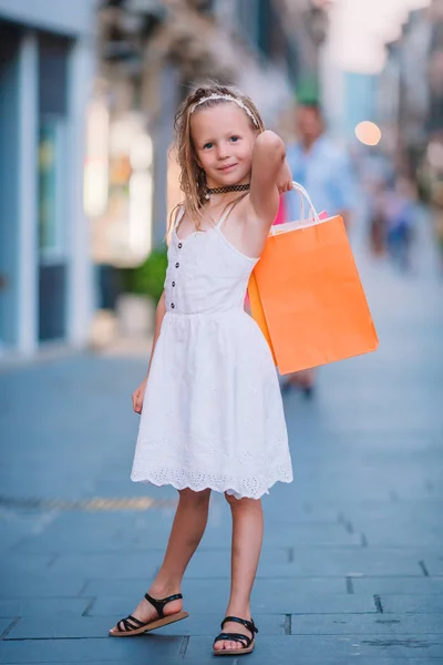 Aranyos kis lány séta a bevásárló táskák, szabadban, európai város portréja. — Stock Fotó