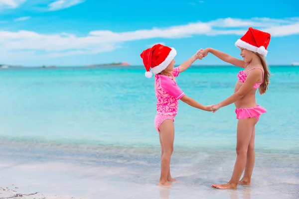 Kleine entzückende Mädchen in Weihnachtsmützen während des Weihnachtsurlaubs am Strand, die zusammen Spaß haben — Stockfoto