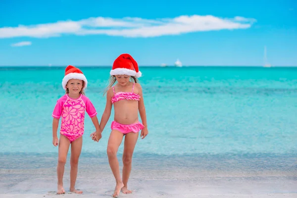 Las niñas adorables en los sombreros de Santa durante las vacaciones de playa se divierten juntas —  Fotos de Stock