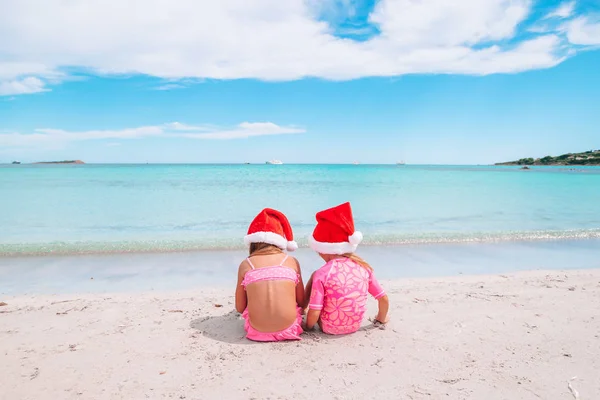 Las niñas adorables en los sombreros de Santa durante las vacaciones de playa se divierten juntas — Foto de Stock