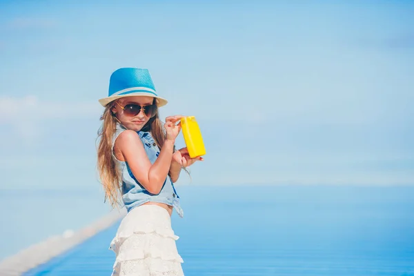 Menina com garrafa de creme solar sentado na borda da piscina — Fotografia de Stock