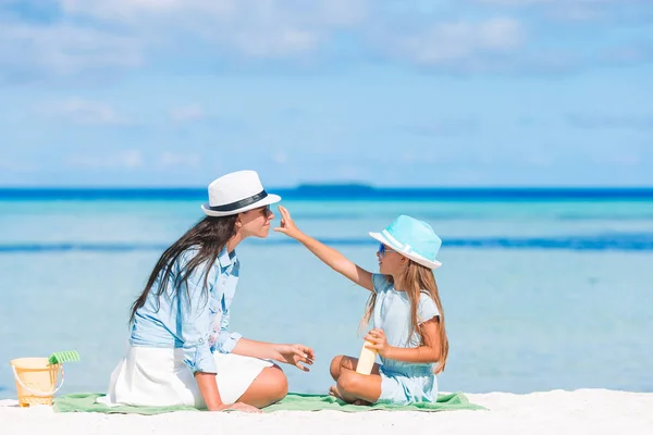 Jonge moeder toepassen zonnebrandcrème aan dochter neus op het strand. — Stockfoto