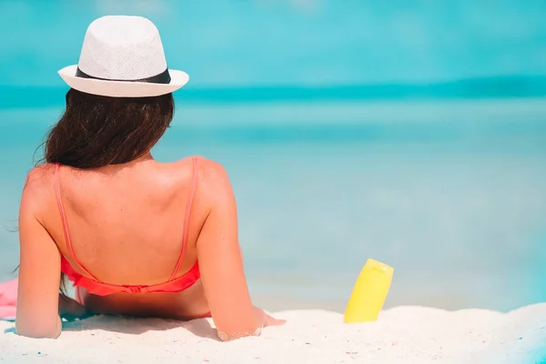 美丽的年轻女子拿着防晒霜躺在热带海滩上 — 图库照片