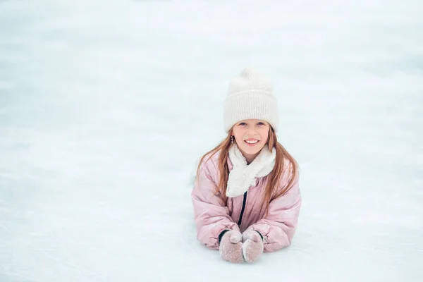 Liten bedårande flicka sitter på isen med skridskor efter fall — Stockfoto