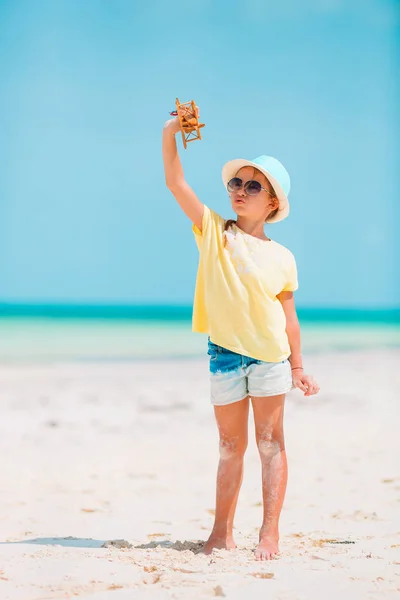 Gelukkig klein meisje met speelgoed vliegtuig in handen op wit zandstrand. — Stockfoto