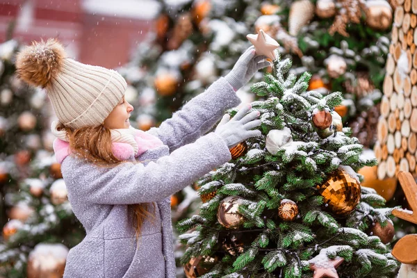 Kleines glückliches Mädchen in der Nähe von Tannenzweig im Schnee für Neujahr. — Stockfoto