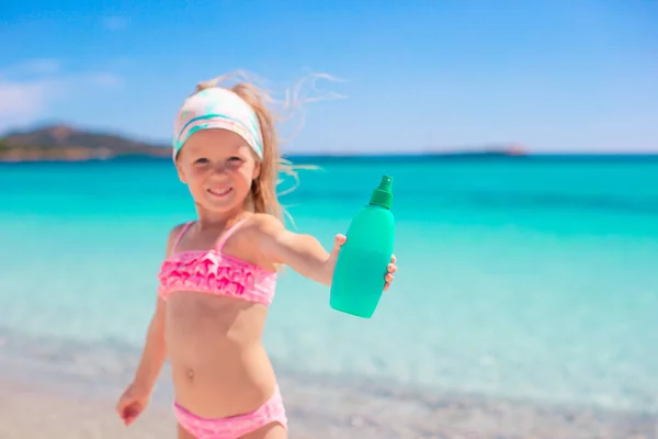 Little girl with bottle of sun cream sitting on the edge of swimming pool — Stock Photo, Image