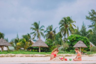 İki çocuk kumdan kale yapıyor ve tropikal sahilde eğleniyor.