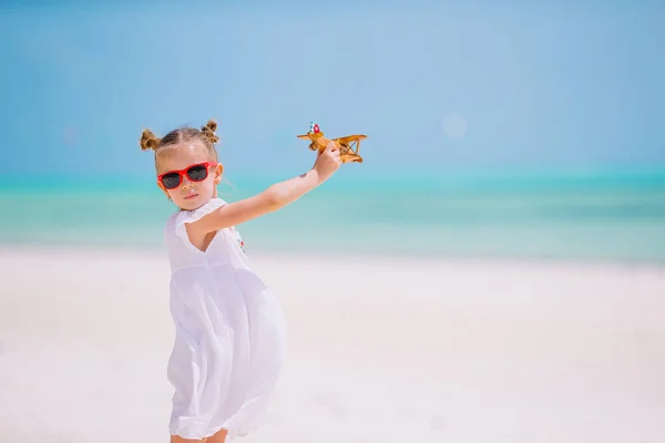 Gelukkig meisje met speelgoed vliegtuig in handen op witte strand — Stockfoto