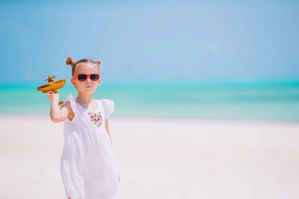 Gelukkig klein meisje met speelgoed vliegtuig in handen op wit zandstrand. — Stockfoto