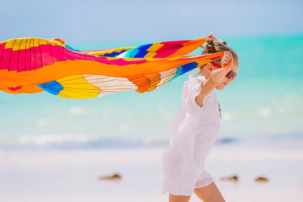 Счастливая маленькая девочка весело бегает с парео на белом пляже — стоковое фото