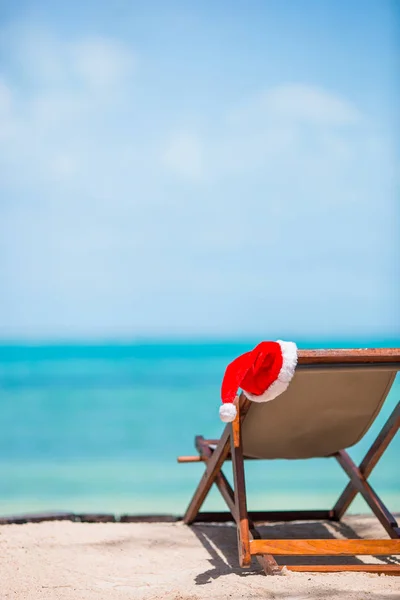 Espreguiçadeiras com chapéu de Santa na bela praia tropical com areia branca e água azul-turquesa. Perfeito Natal férias — Fotografia de Stock