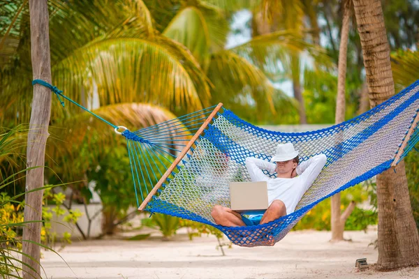 Jongeman met laptop bij hangmat op tropische vakantie — Stockfoto