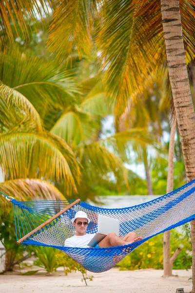 Hombre joven con el ordenador portátil en la hamaca en vacaciones tropicales — Foto de Stock
